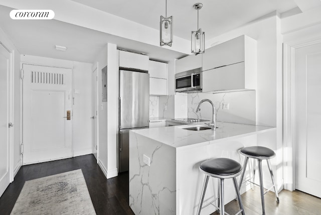 kitchen with white cabinetry, kitchen peninsula, appliances with stainless steel finishes, decorative light fixtures, and sink