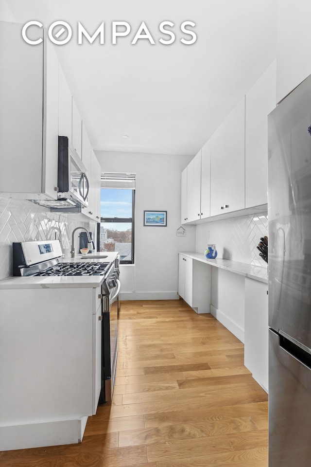 kitchen with light wood-style floors, appliances with stainless steel finishes, white cabinets, and light countertops