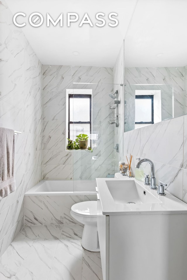 full bath featuring stone wall, toilet, vanity, tile walls, and marble finish floor