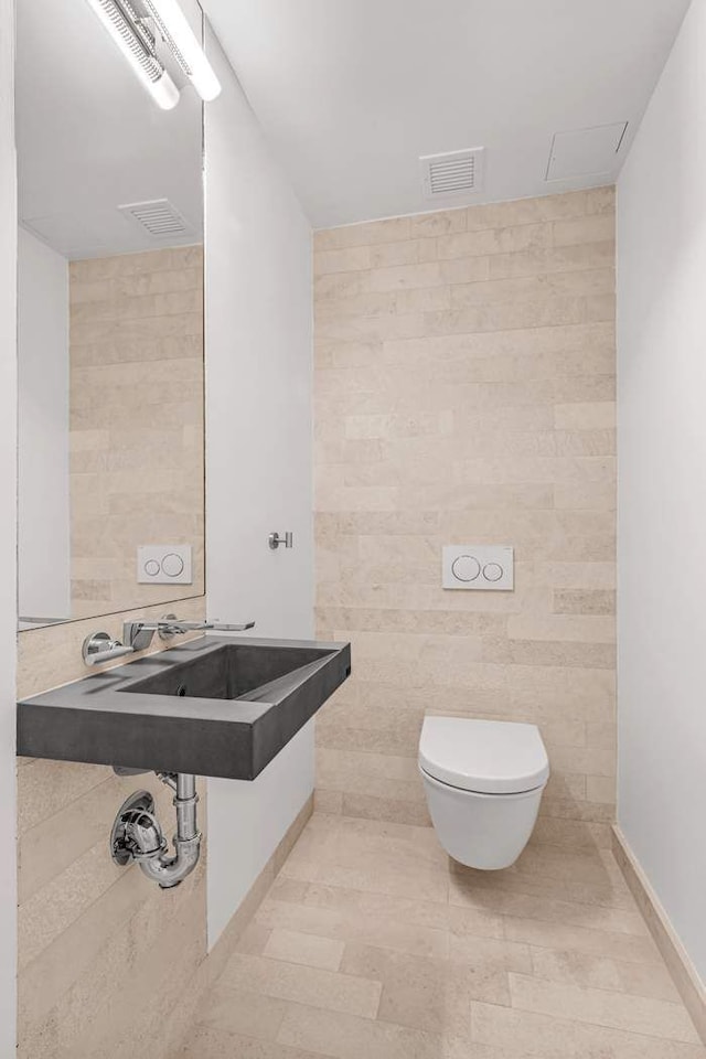 bathroom with toilet, a sink, visible vents, and tile walls