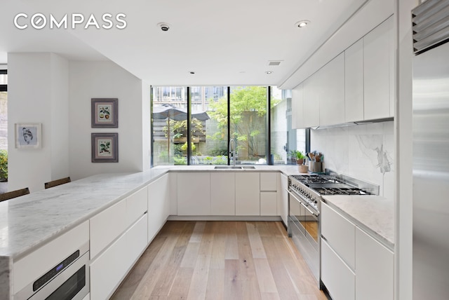 429 Kent Ave Unit Th2, New York City, NY 11249 - kitchen featuring stainless steel appliances, a sink, modern cabinets, light wood-style flooring, and white cabinetry