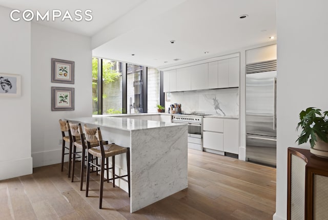 kitchen featuring a breakfast bar, white cabinets, light wood-style flooring, and high quality appliances