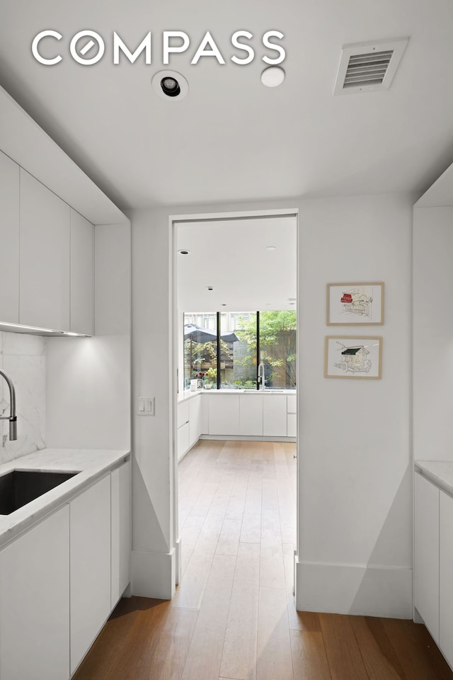 kitchen featuring light wood finished floors, visible vents, white cabinets, and a sink