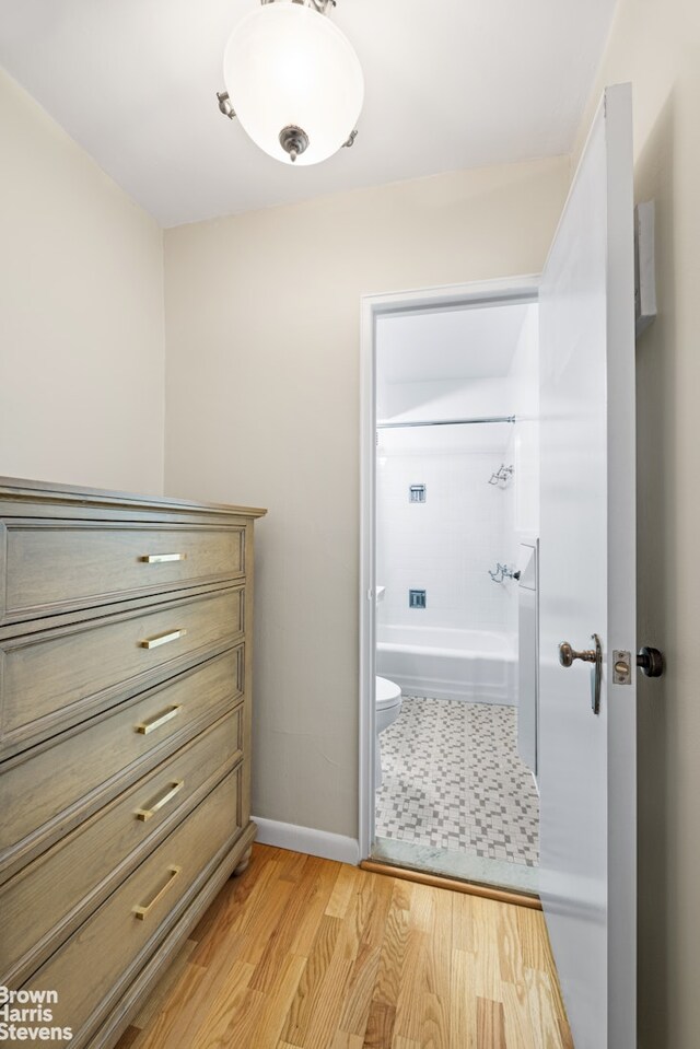 bathroom with a tub to relax in, toilet, and hardwood / wood-style floors