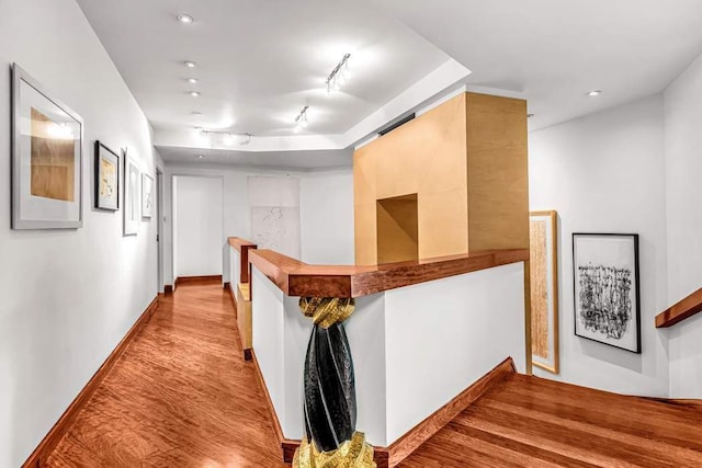 hallway with a barn door, baseboards, wood finished floors, an upstairs landing, and track lighting