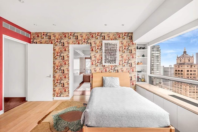 bedroom with visible vents, wood finished floors, and wallpapered walls