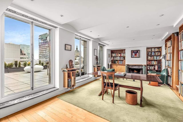 office featuring a lit fireplace, a city view, built in shelves, and hardwood / wood-style flooring