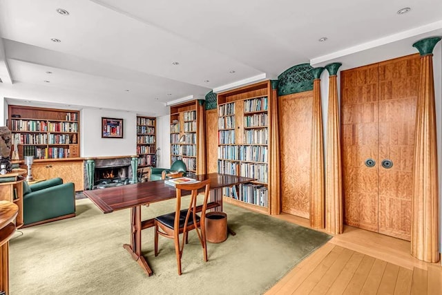 office area with a warm lit fireplace, wall of books, and wood finished floors