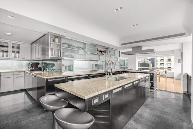 kitchen featuring wall chimney exhaust hood, light stone counters, a sink, stainless steel appliances, and decorative backsplash