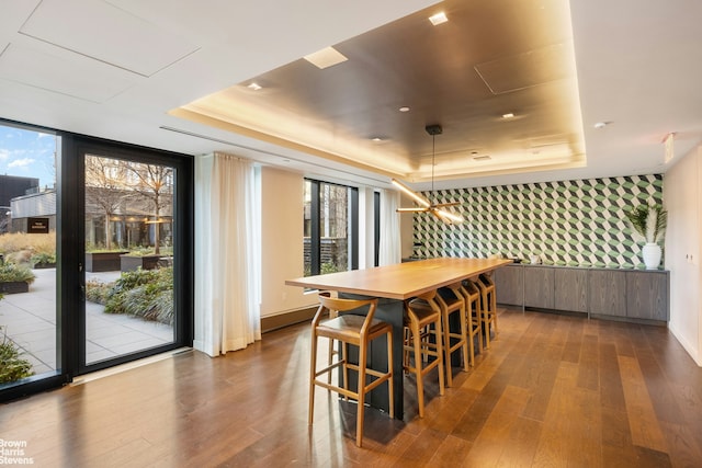 dining space with dark wood-type flooring, a raised ceiling, floor to ceiling windows, and wallpapered walls