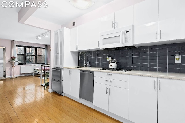 kitchen with white cabinets, backsplash, appliances with stainless steel finishes, and light hardwood / wood-style floors