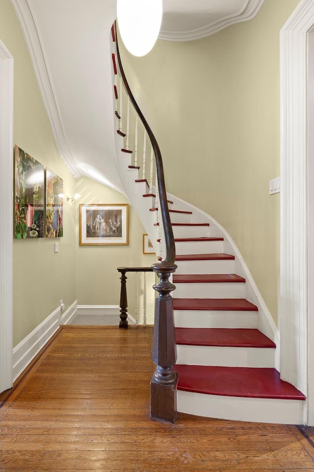 staircase with ornamental molding, wood finished floors, and baseboards