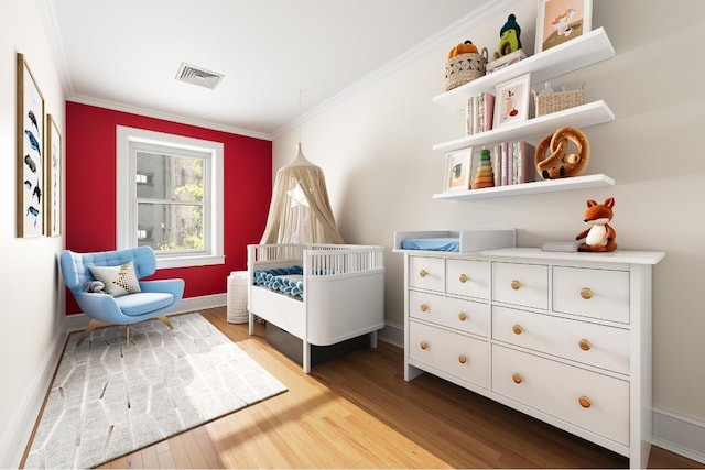 bedroom featuring crown molding, light hardwood / wood-style flooring, and a crib