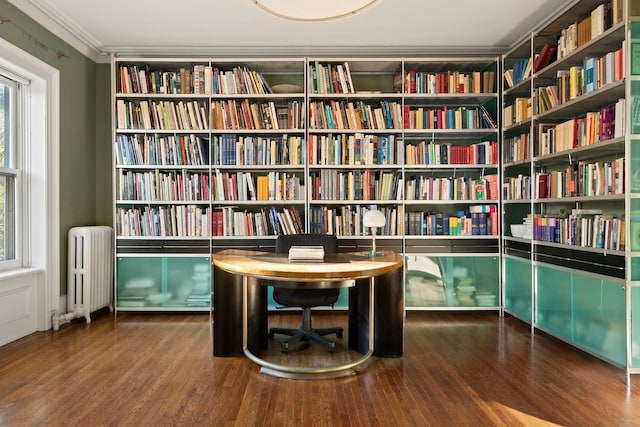 unfurnished room featuring radiator, wall of books, ornamental molding, and wood finished floors