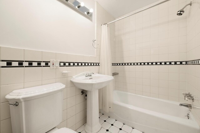 full bath featuring tile walls, toilet, a wainscoted wall, shower / tub combo with curtain, and a sink