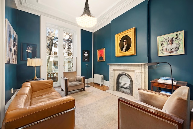 living area featuring radiator, a premium fireplace, wood finished floors, crown molding, and a chandelier