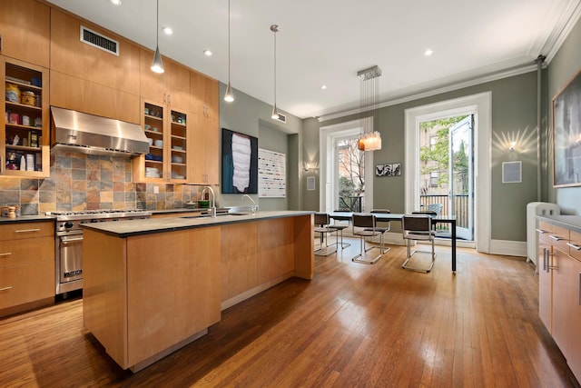 kitchen featuring tasteful backsplash, visible vents, premium stove, a kitchen island with sink, and wall chimney range hood