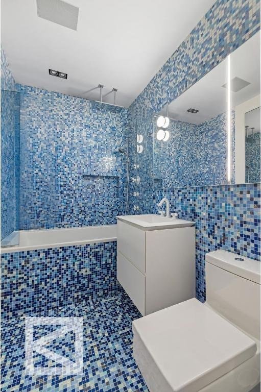 bathroom with toilet, a tub to relax in, tile patterned flooring, tile walls, and vanity