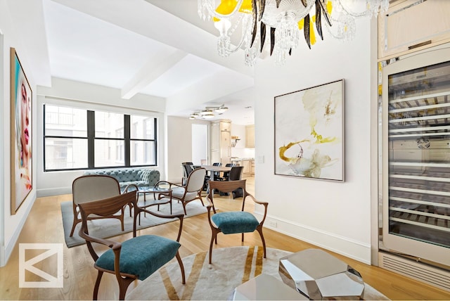 sitting room with baseboards, wine cooler, a chandelier, beamed ceiling, and light wood-style flooring