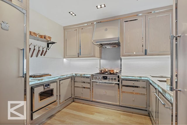 kitchen featuring light hardwood / wood-style floors, tasteful backsplash, fridge, custom range hood, and high end range