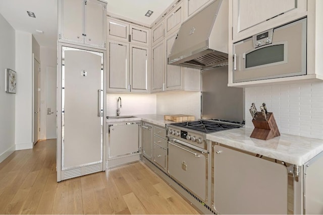 kitchen featuring light hardwood / wood-style floors, paneled built in refrigerator, stainless steel gas cooktop, light stone counters, and sink