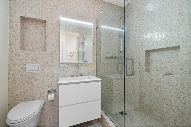 bathroom featuring tile walls, toilet, walk in shower, and vanity