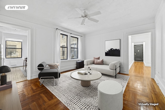 living area featuring a ceiling fan, radiator heating unit, visible vents, and a decorative wall