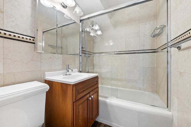 full bathroom with tile walls, shower / bath combination with glass door, vanity, and toilet