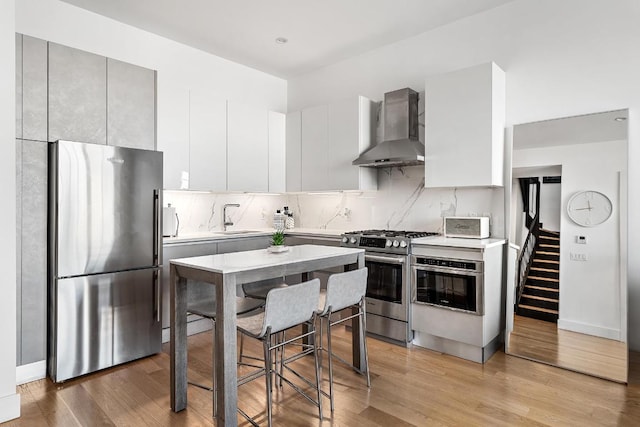 kitchen featuring wall chimney exhaust hood, sink, light wood-type flooring, stainless steel appliances, and white cabinets