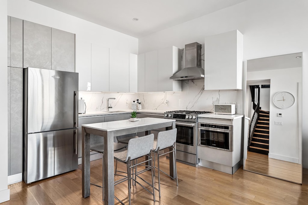 kitchen featuring a sink, appliances with stainless steel finishes, wall chimney exhaust hood, and light wood finished floors