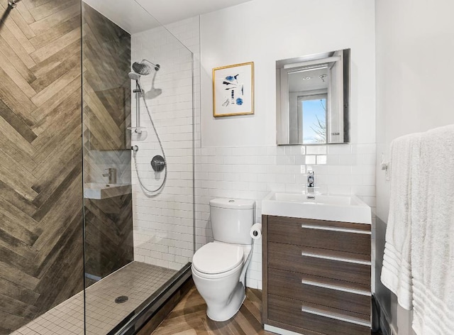 bathroom with a shower with door, vanity, tile walls, and toilet