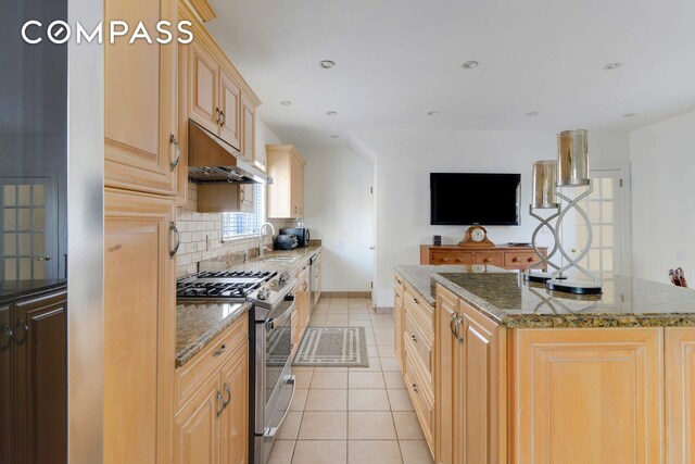 139 82nd St, New York City, NY 11209 - kitchen with stainless steel gas range, under cabinet range hood, decorative backsplash, light tile patterned flooring, and a center island with sink