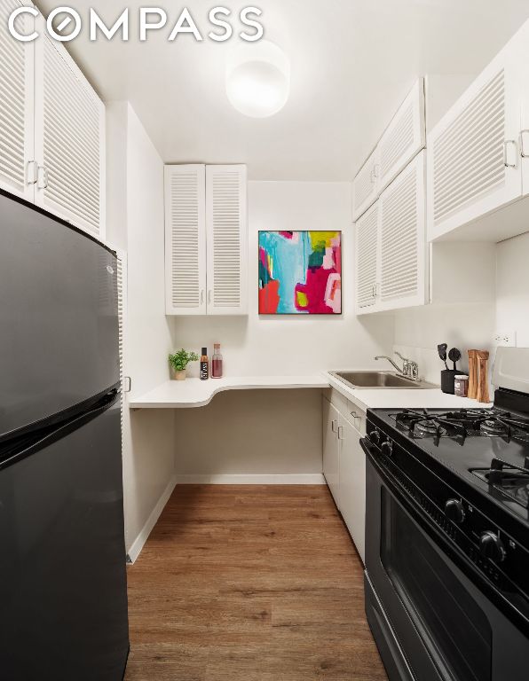 kitchen with white cabinetry, sink, hardwood / wood-style flooring, stainless steel refrigerator, and gas range