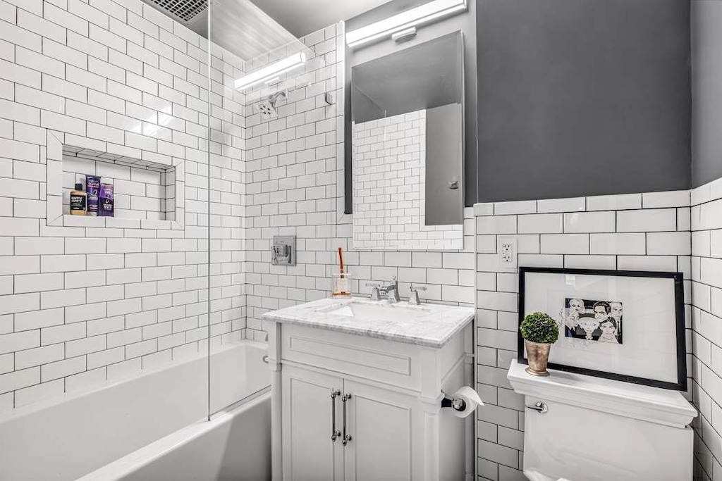 full bathroom with tile walls, vanity, tiled shower / bath, and toilet