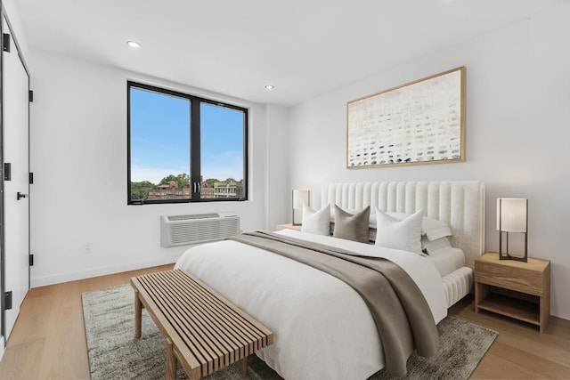 bedroom featuring light wood-style floors, recessed lighting, a wall unit AC, and baseboards