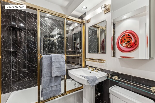 225 E 57th St Unit 7G, New York City, NY 10022 - full bath featuring toilet, shower / bath combination with glass door, recessed lighting, tile walls, and a sink