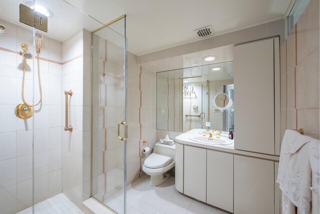 bathroom featuring toilet, vanity, tile walls, tile patterned floors, and a shower with shower door