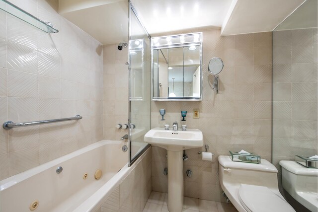 full bathroom featuring toilet, tile patterned flooring, a combined bath / shower with jetted tub, and tile walls