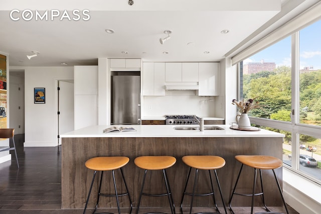 kitchen with high end refrigerator, modern cabinets, light countertops, under cabinet range hood, and white cabinetry