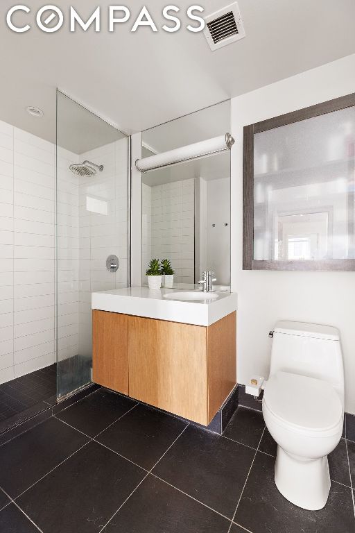 bathroom featuring toilet, tile patterned floors, tiled shower, and vanity