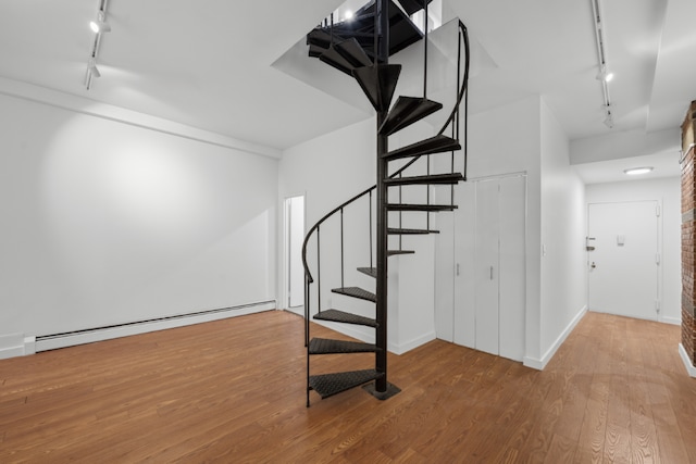 stairway with a baseboard heating unit, wood-type flooring, and rail lighting