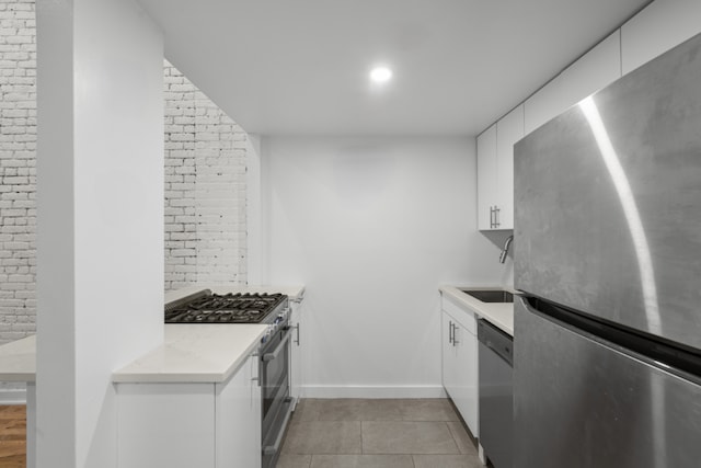 kitchen featuring light tile patterned flooring, brick wall, sink, white cabinets, and stainless steel appliances