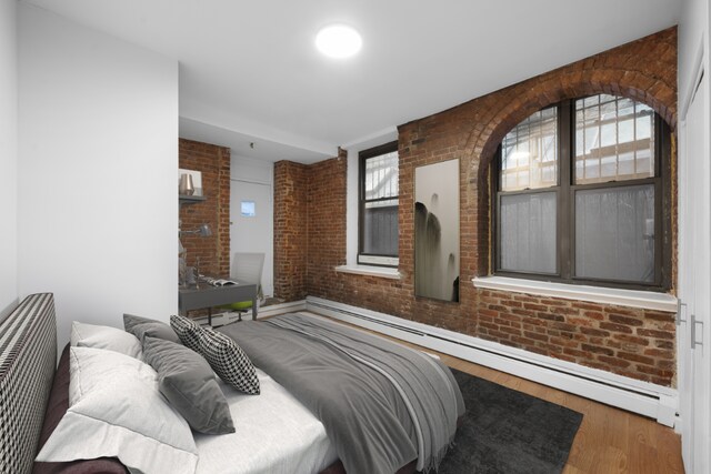 bedroom featuring a baseboard heating unit, hardwood / wood-style flooring, and brick wall