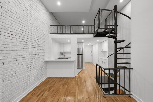 interior space with white cabinetry, light wood-type flooring, stainless steel fridge, a towering ceiling, and brick wall