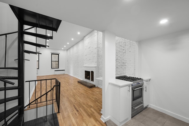 kitchen featuring brick wall, high end stove, white cabinetry, a large fireplace, and light hardwood / wood-style flooring