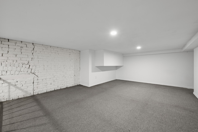 basement featuring dark carpet and brick wall