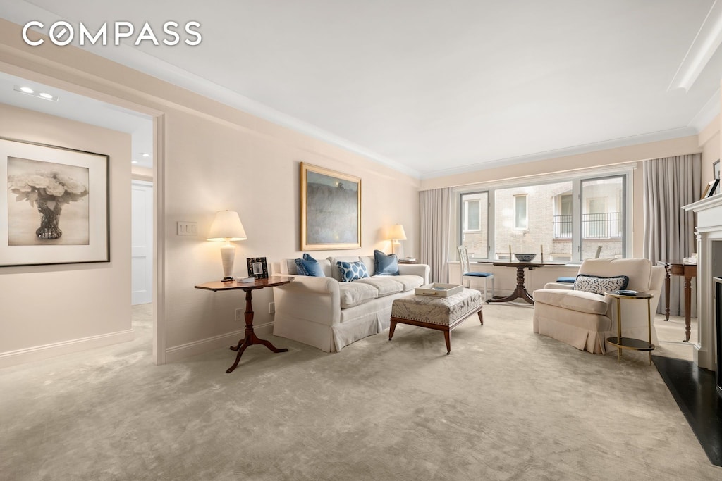 carpeted living area with crown molding, a fireplace with raised hearth, and baseboards