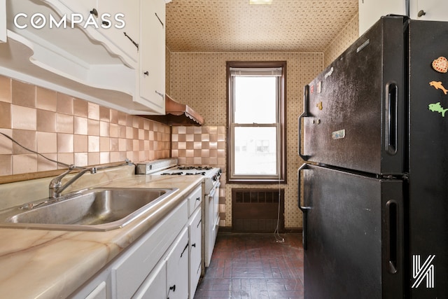 kitchen featuring light countertops, freestanding refrigerator, white range with gas stovetop, and white cabinetry