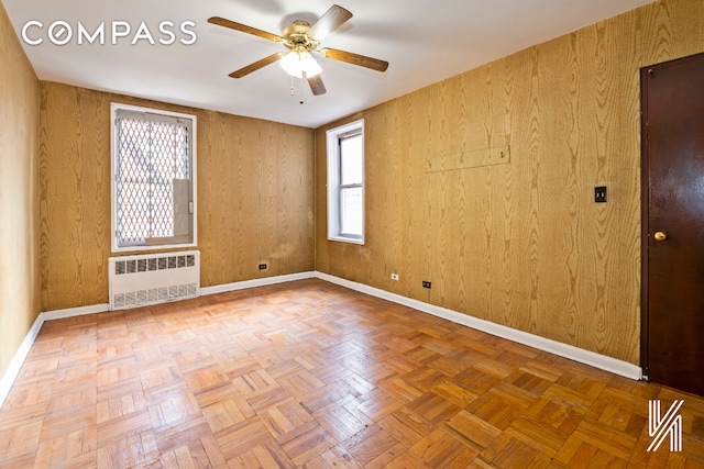 empty room featuring radiator heating unit, a ceiling fan, and baseboards