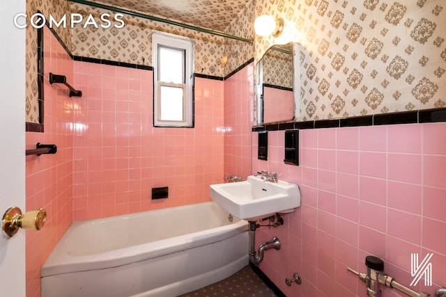 full bathroom featuring wainscoting, a sink, tile walls, and wallpapered walls